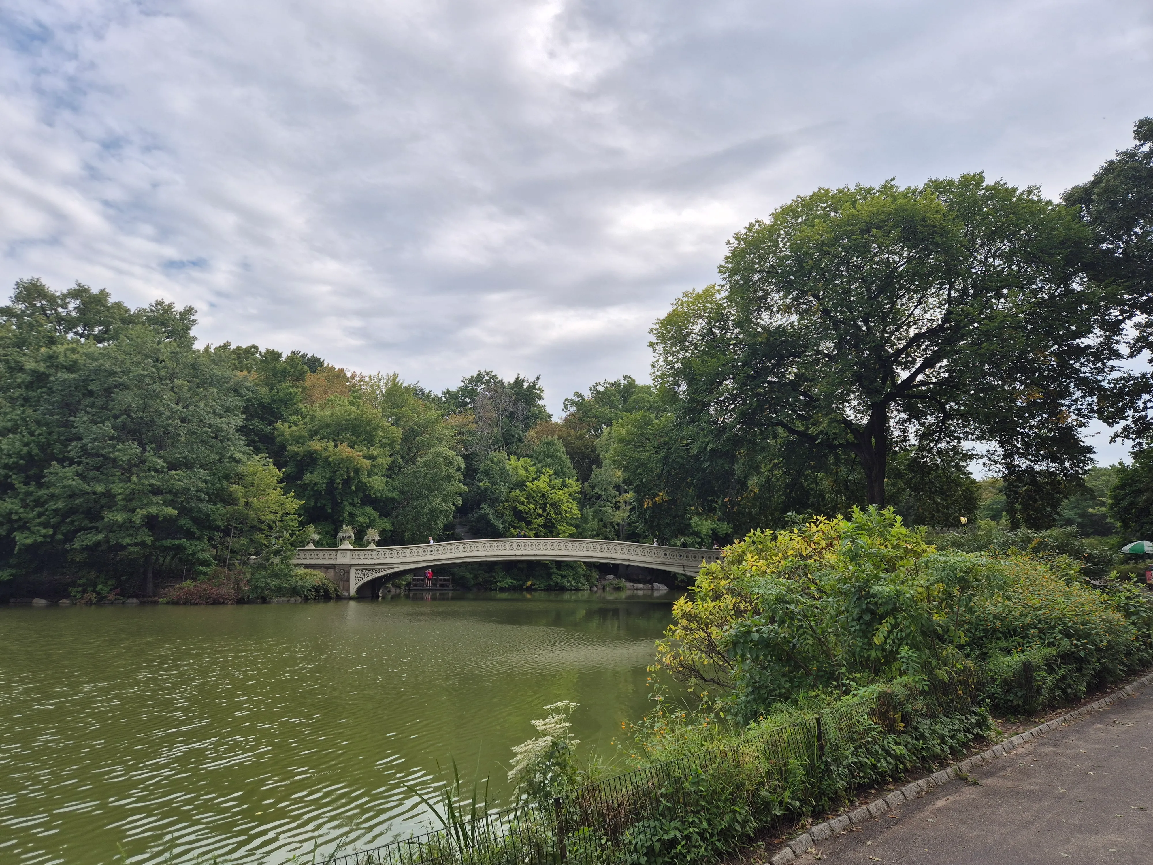 A stone bridge over a lake surrounded by green trees